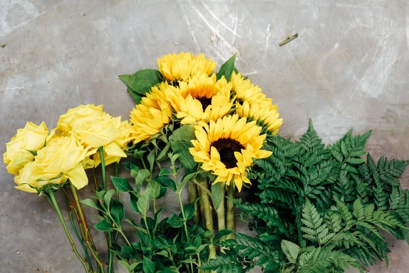 preparacion de un ramo con rosas amarillas girasoles y helecho en una mesa