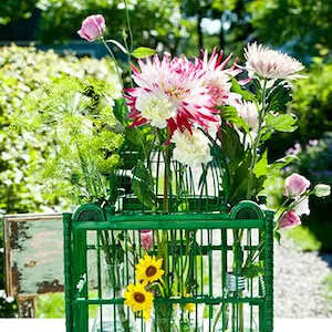 una jaula de flores en una mesa de un jardin con dalias crisantemos y lisianthus
