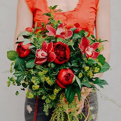 un ramo de flores compuesto por peonias rojas y orquideas cymbidium rojos