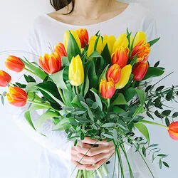 chica con una ramo de tulipanes amarillos y naranjas con eucalipto