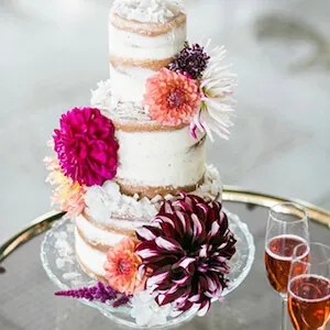 una tarta blanca decorada con dahlias de color morado naranja y fuschia
