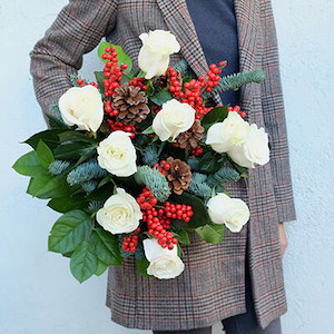 un ramo de flores con ilex rojo y rosas blancas con piñas