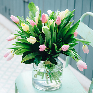 ramo de tulipanes rosas y amarillas en un jarron de cristal encima de una silla